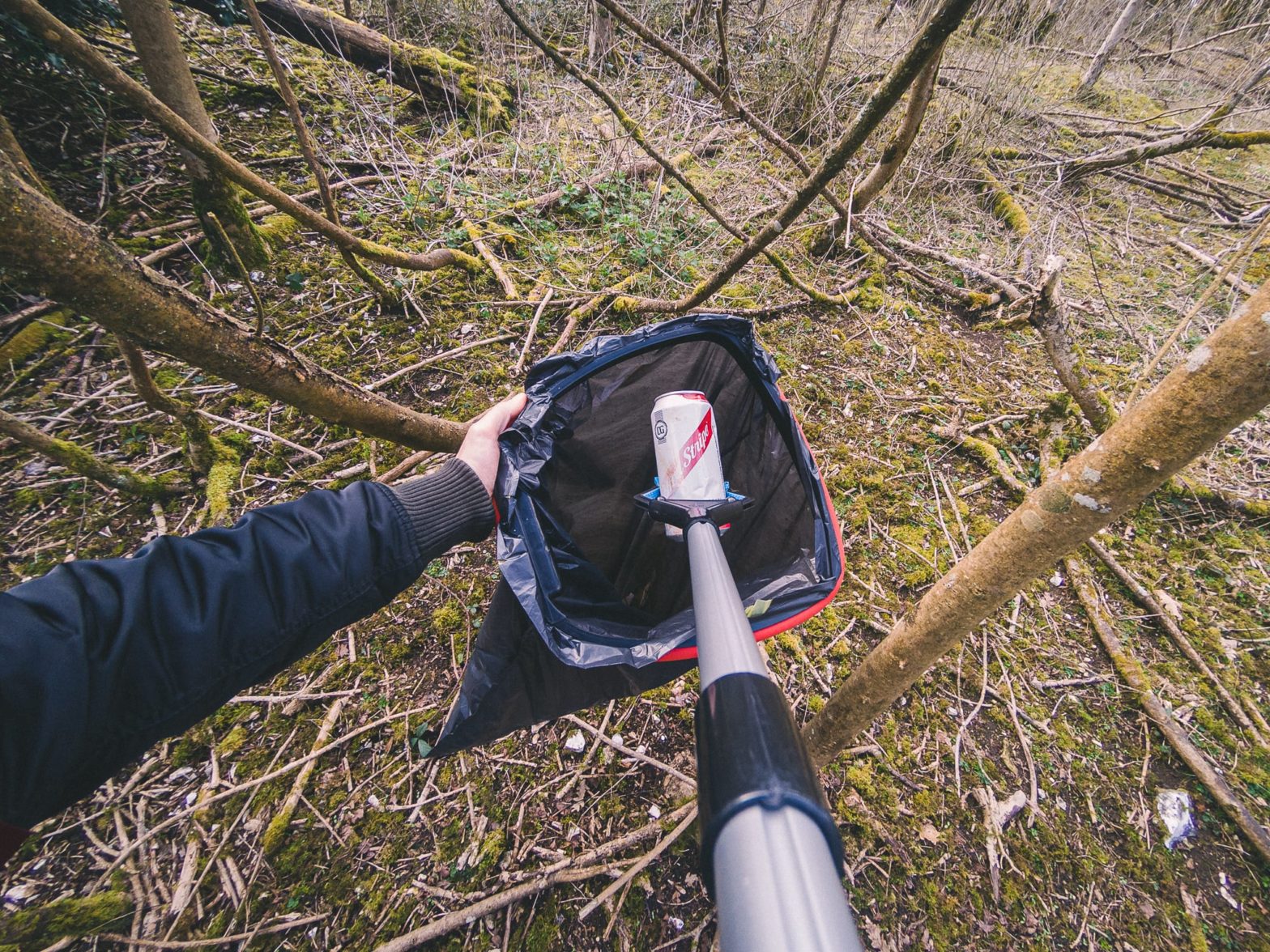 A discarded aluminium can in a forest being placed in a bag with a litter picker