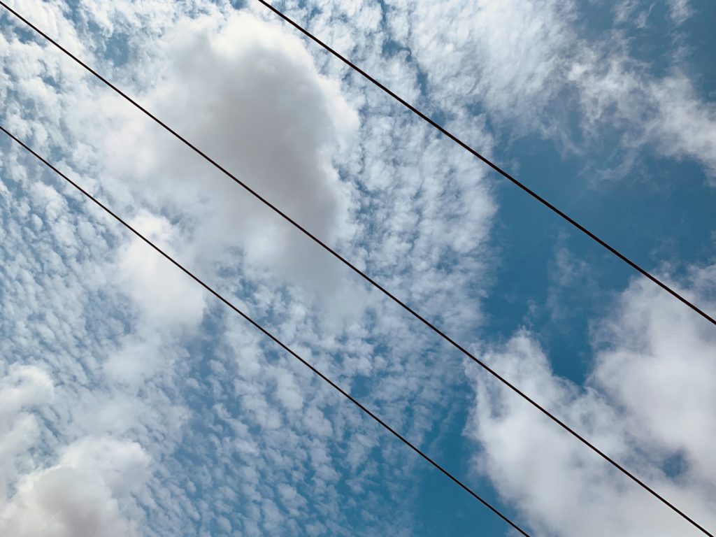 Clouds in the bright blue sky divided by 3 power lines running diagonally from top left to bottom right