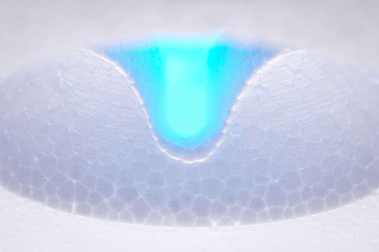 A closeup of styrofoam with perforations forming a pattern in the middle and blue light shining through the middle