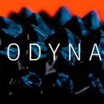 Close up of ferrofluid forming peaks in response to a magnetic field agains a bright orange background with a word "Hydrodynamics" written across