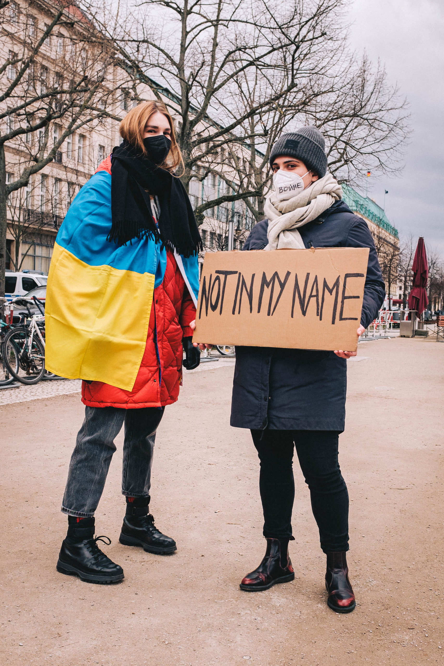 A protester draped in Ukrainian flag talking to another with a sign that reads: "NOT IN MY NAME" outside the russian embassy in Berlin