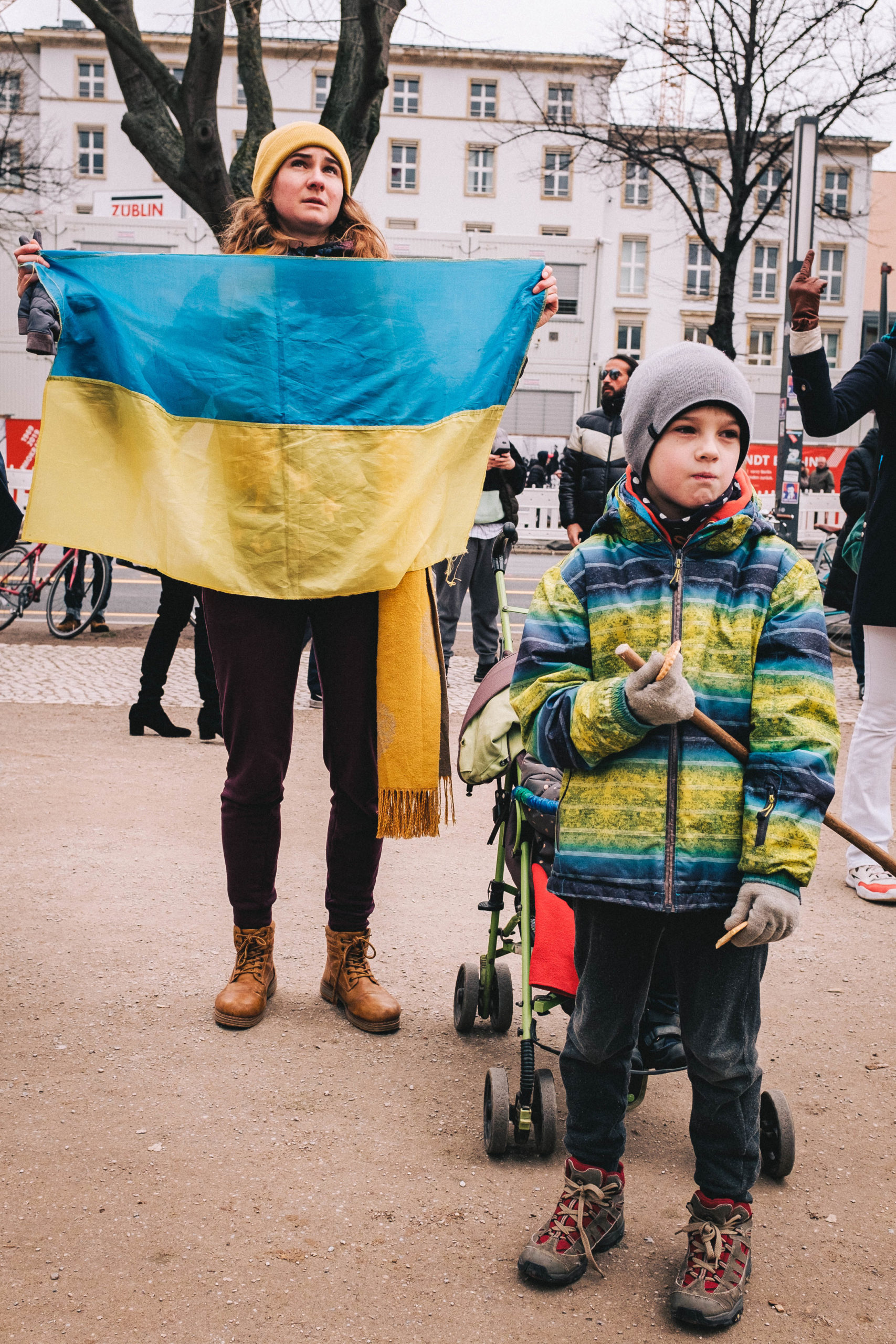 A woman holding up Ukrainian flag with a kid outside the russian embassy in Berlin