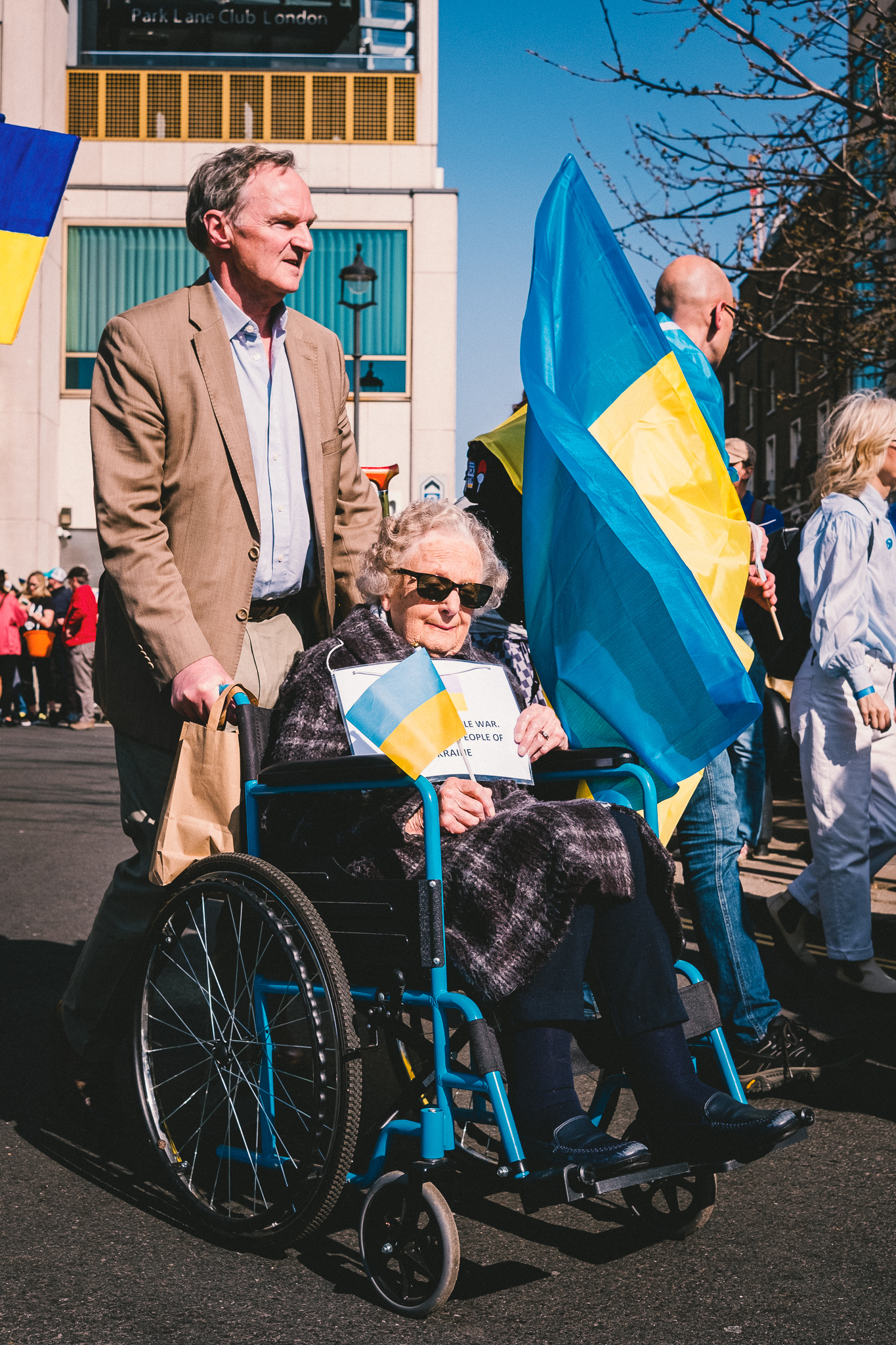 An elderly lady in a wheelchair arriving at the protest with a male companion