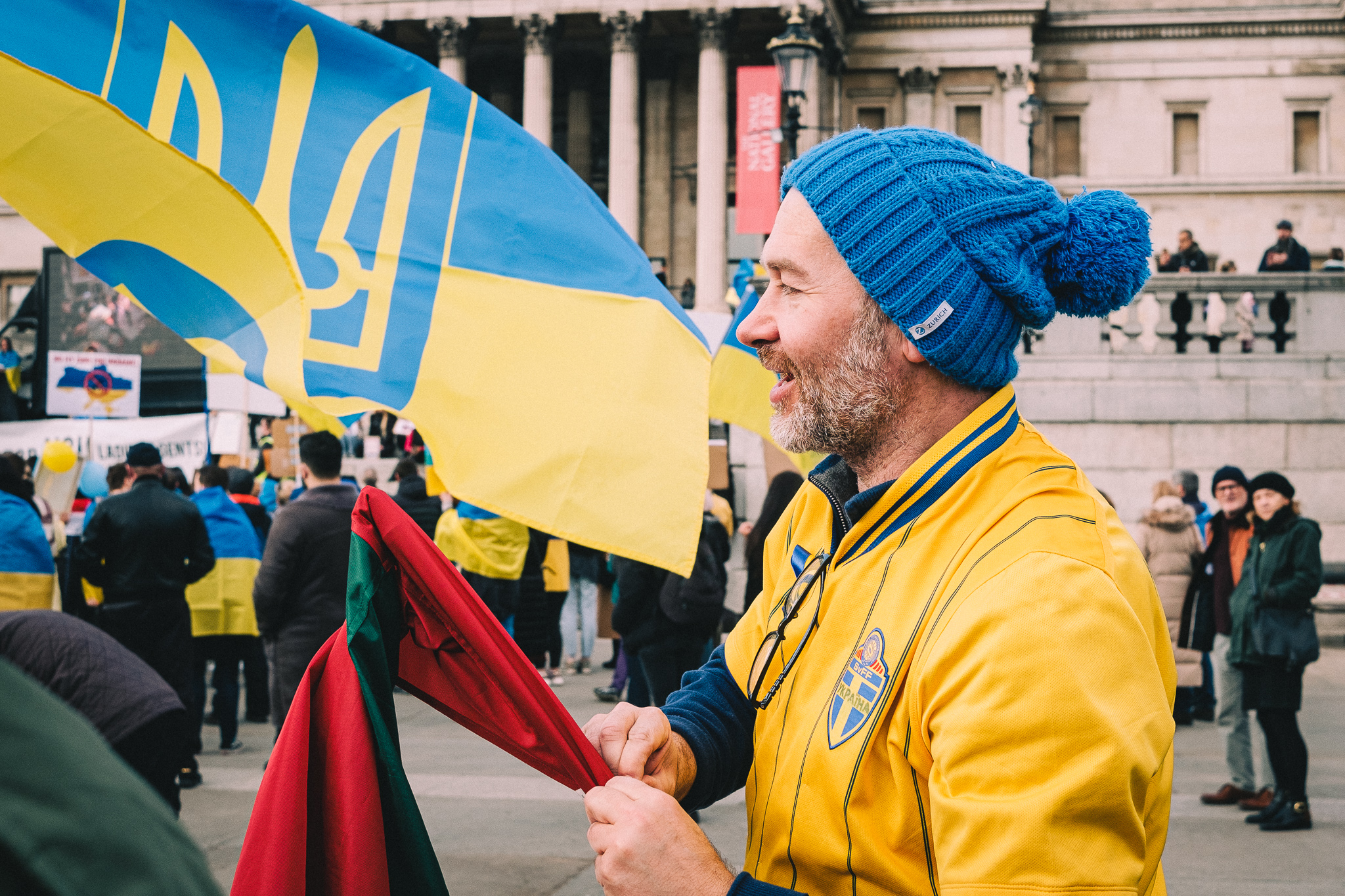 A protester putting up a flag at the rally to support Ukraine at Trafalgar Square wearing yellow top and a blue hat