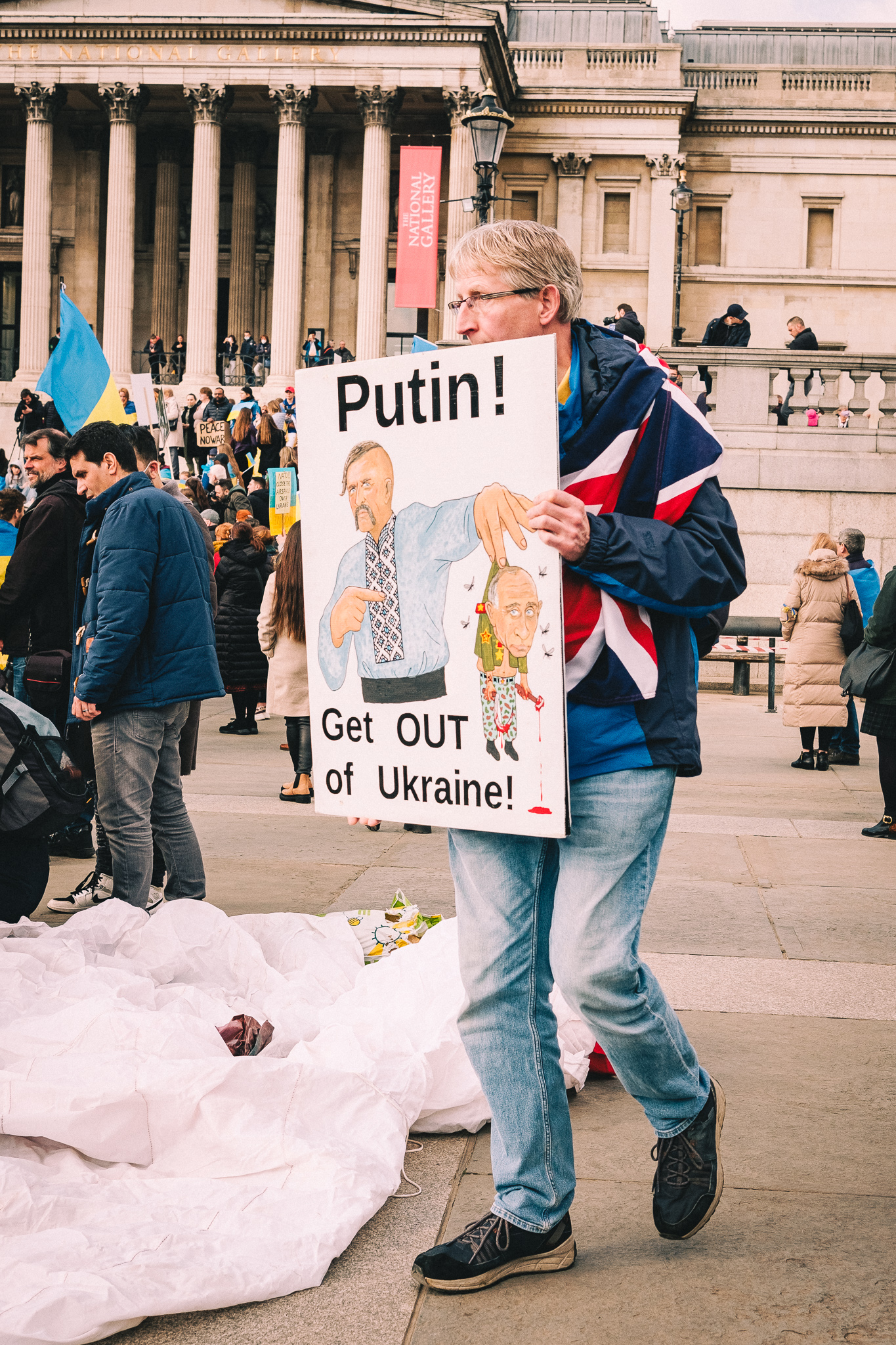 A protester holding a sign: "Putin! Get OUT of Ukraine!" depicting a Ukrainian Cossack picking up Putin holding a bloody tool