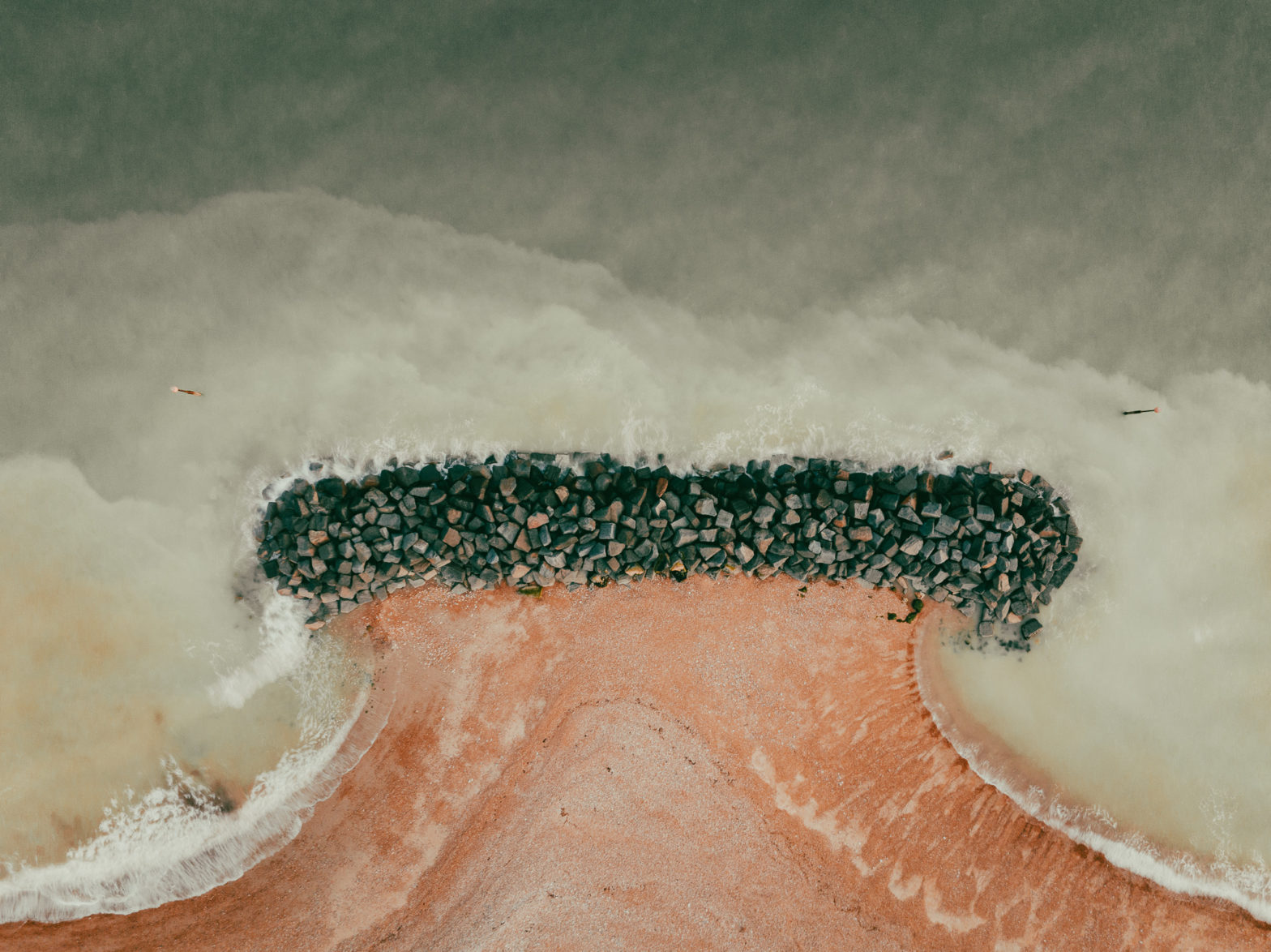 Top down view of a wave breaker by the beach constructed of large dark stones