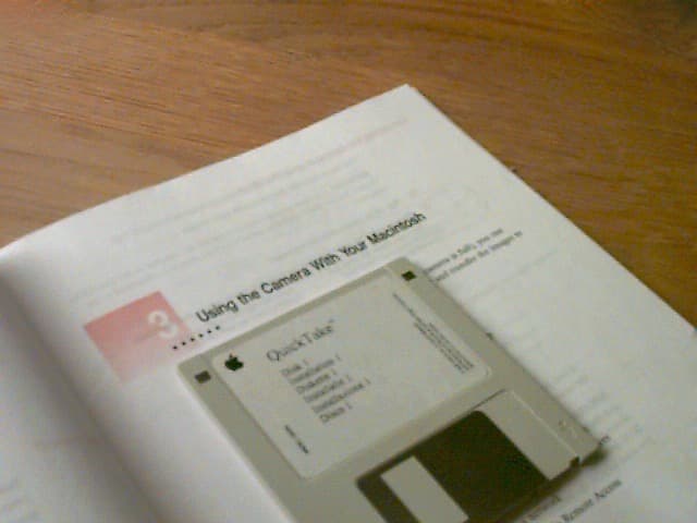 QuickTake 100 user manual open at Using the Camera With Your Macintosh chapter and a QuickTake software floppy disk next to it