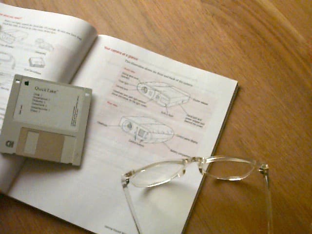QuickTake 150 user manual showing a camera diagram next to clear plastic glasses and a floppy disk