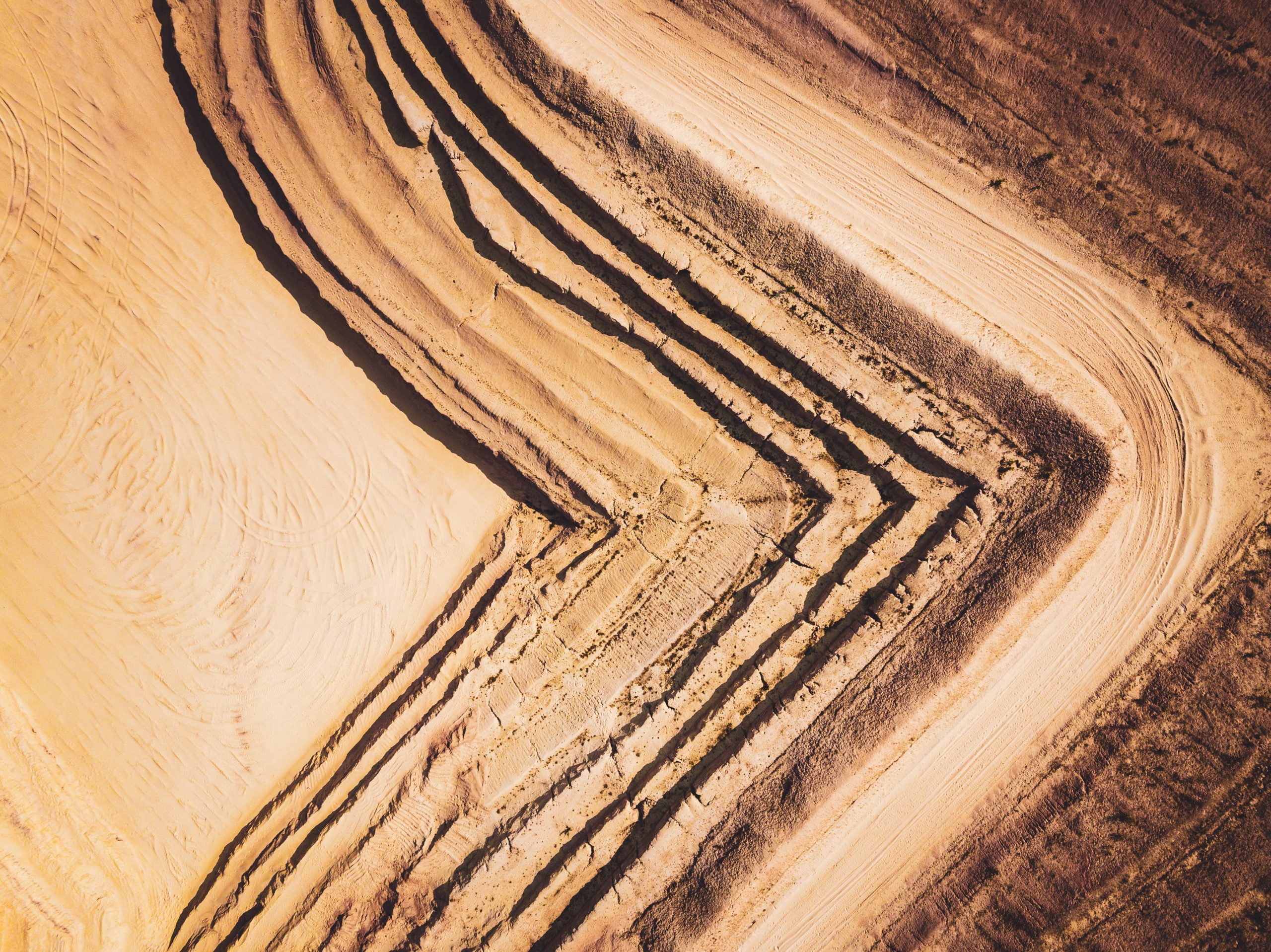 Top down aerial photo of a sand quarry with different layers descending down forming triangular shapes at 90° angles