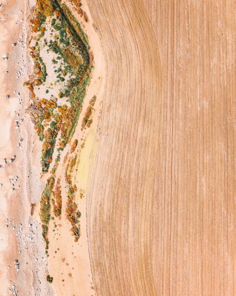 Top down aerial view of a ploughed field by the beach with curved and straight lines visible in the tilted soil created by the heavy machinery, resembling a Japanese zen garden