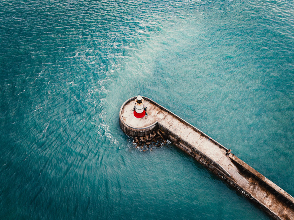 Aerial photo of a concrete wall extending far in to the sea with a lighthouse on the end
