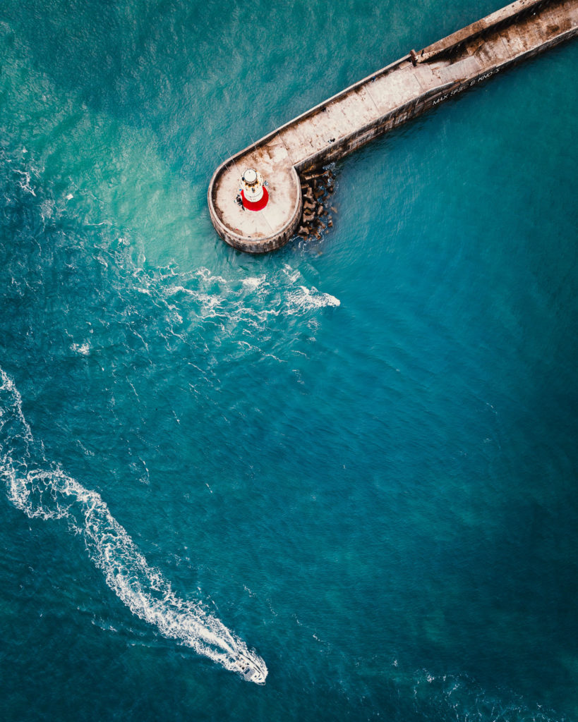 Aerial photo of a concrete wall extending far in to the sea and a motorboat sailing by